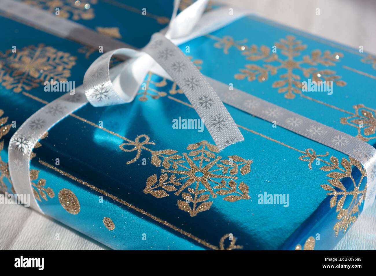 Beautifully wrapped snowflake themed turquoise Christmas present decorated with a white bow on a plain white background Stock Photo