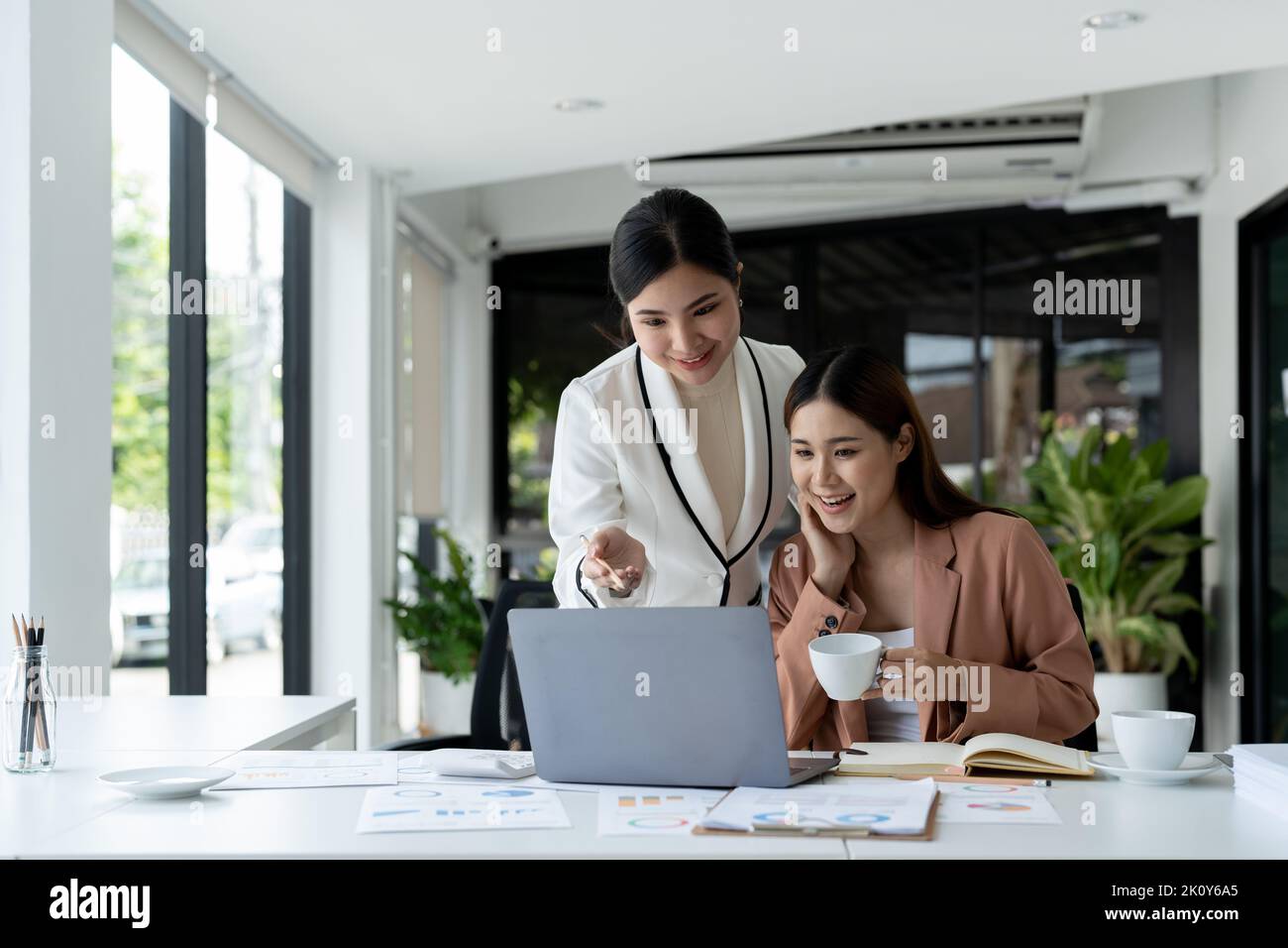 Two asian business partnership coworkers discussing a financial planning graph and company during a budget meeting in office room. Stock Photo