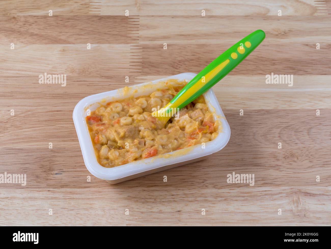 Macaroni and cheese baby food with a spoon in the food on a wood tabletop illuminated with natural light. Stock Photo