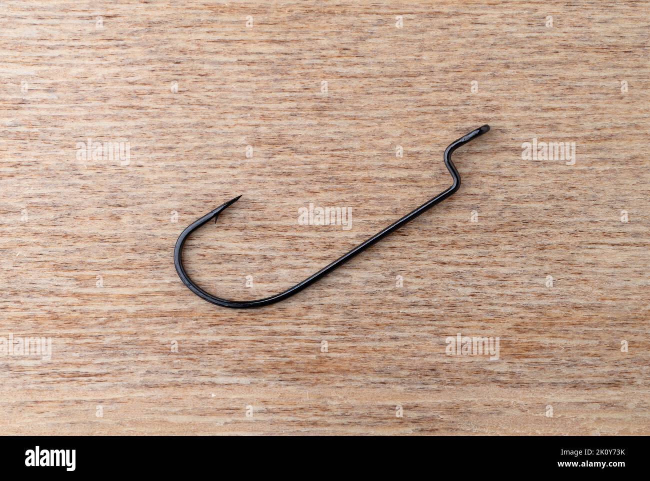 Top view of a single offset plastic worm bait hook on a wood background. Stock Photo