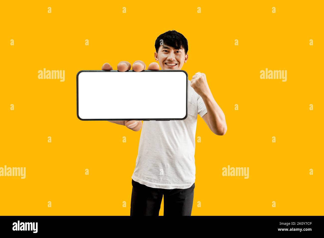 Asian Man Holding Smartphone With Empty White Screen On Yellow Background. Cellphone display Mockup for Mobile App Advertisement. Stock Photo