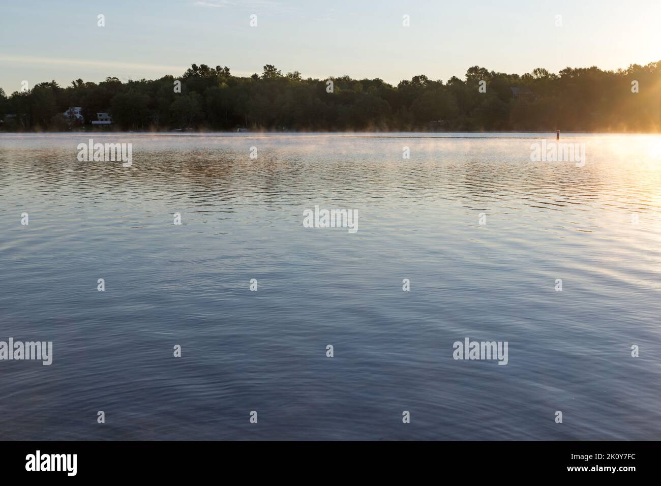 Fog rising on Swan Lake in Maine in the early fall with distant shoreline. Stock Photo
