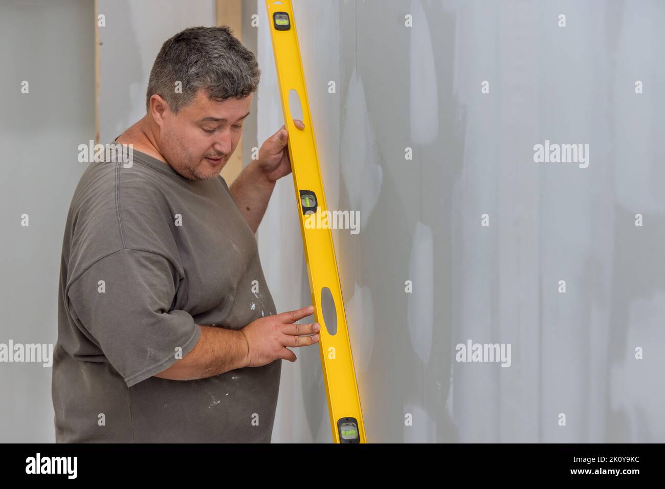 In order to ensure that a wall of drywall is level before it is painted, the employee uses a level Stock Photo
