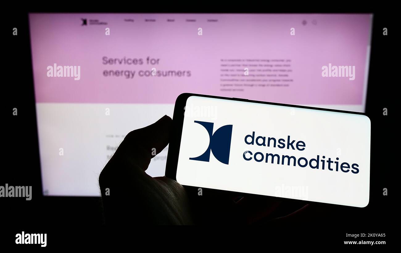 Person holding smartphone with logo of energy trading company Danske Commodities AS on screen in front of website. Focus on phone display. Stock Photo