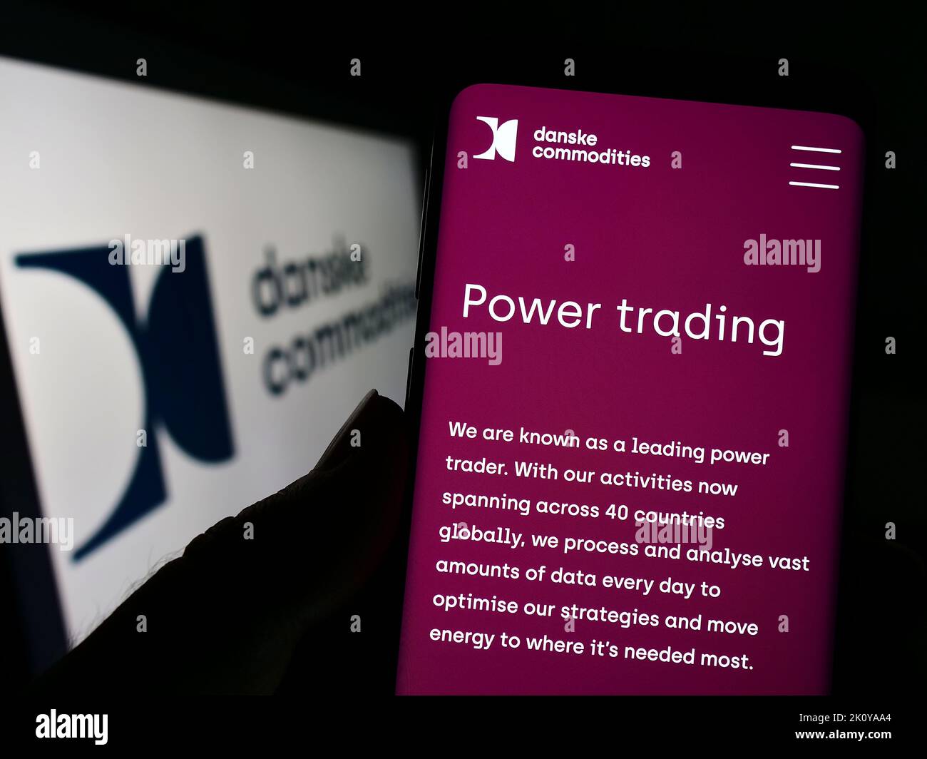 Person holding cellphone with webpage of energy trading company Danske Commodities AS on screen in front of logo. Focus on center of phone display. Stock Photo
