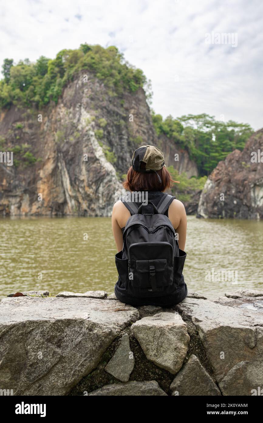 A rear view of a female looking the cliff view while sitting on a rock ...