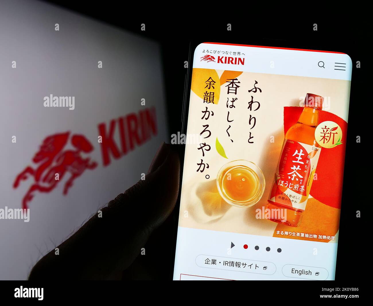 Person holding cellphone with website of Japanese Kirin Brewery Company Limited on screen in front of logo. Focus on center of phone display. Stock Photo
