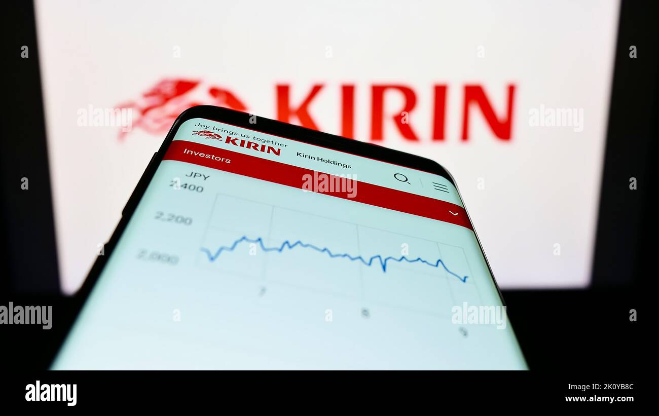 Mobile phone with webpage of Japanese Kirin Brewery Company Limited on screen in front of business logo. Focus on top-left of phone display. Stock Photo