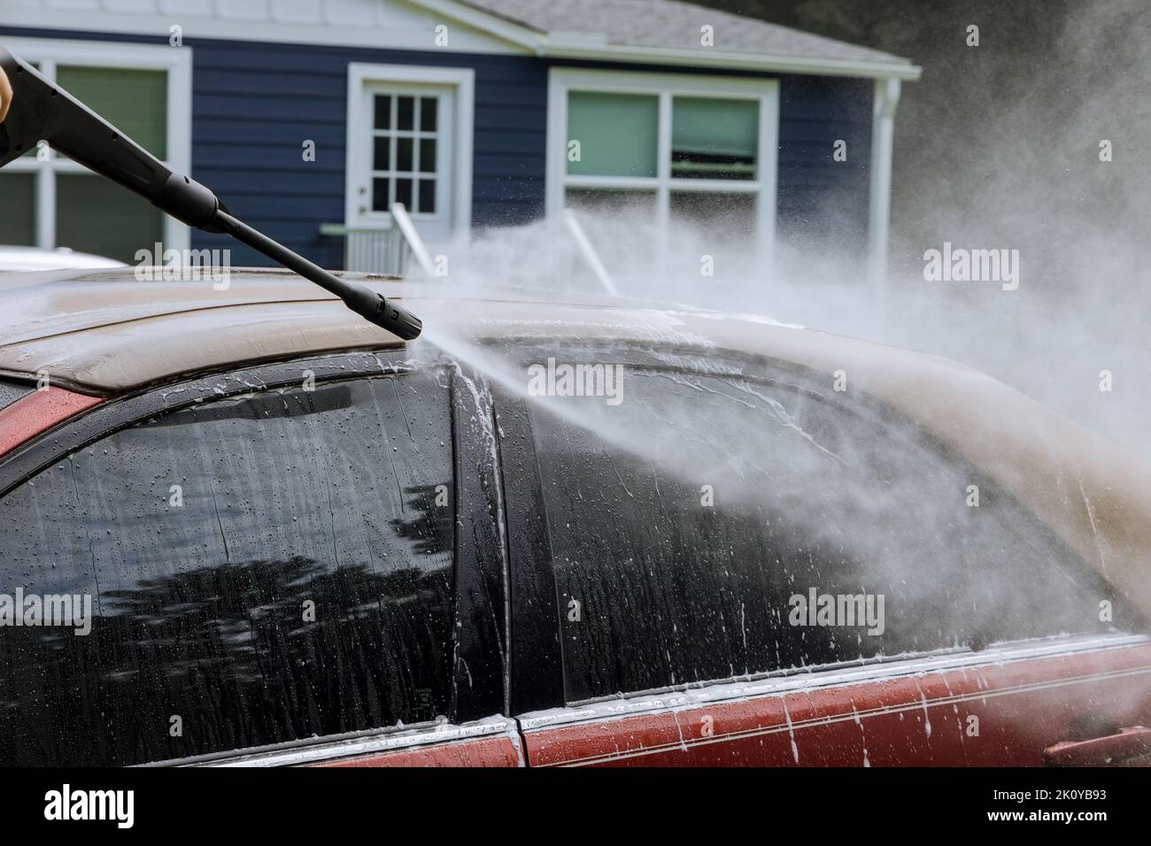 Man is washing his car under the high pressure jet spraying water with the purpose of cleaning the car Stock Photo