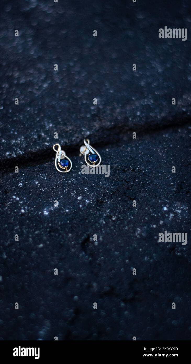 A selective focused picture of a pair of gold diamond and sapphire earrings in a black background Stock Photo