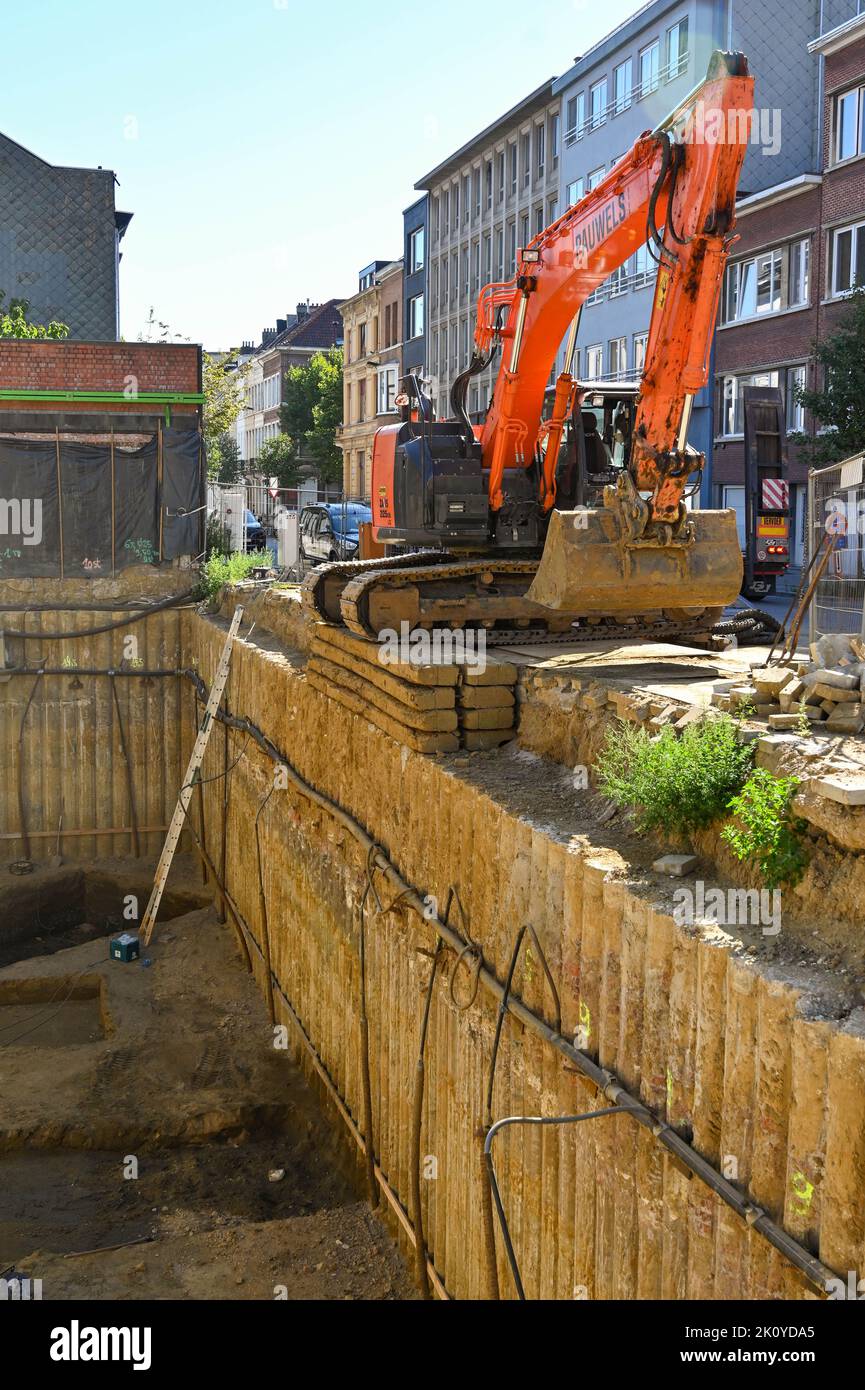 Antwerp, Belgium - August 2022: Mechanical digger parked on the edge of a large hole prepared for the foundations of a new building Stock Photo