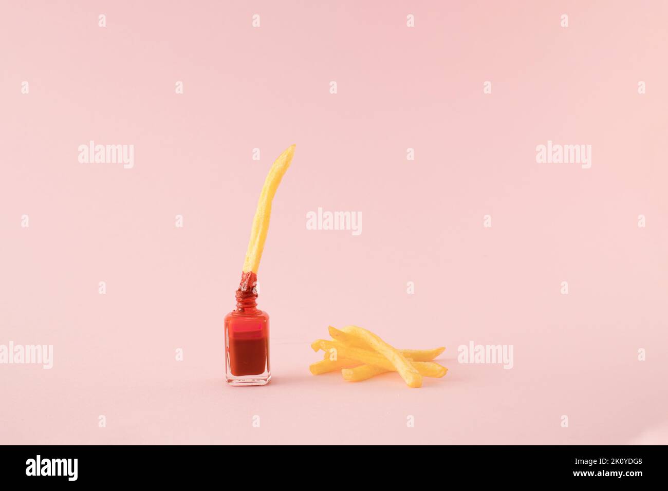 French fried potato dipped in red nail polish with a pile of fries on the side on pink background. Minimal concept. Stock Photo