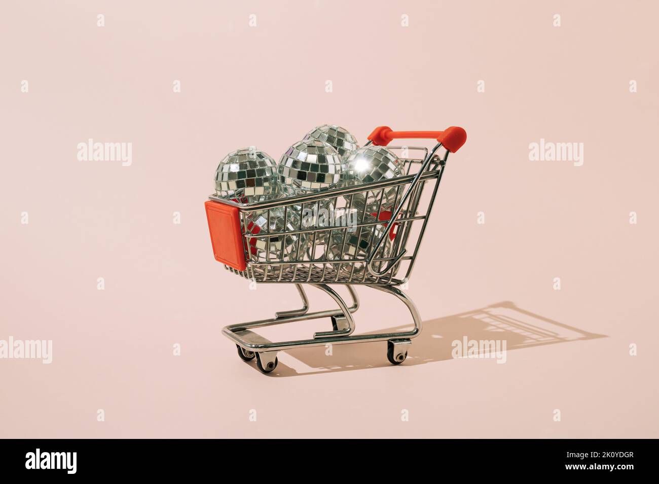 Shopping cart full of disco balls on pink background. Minimal concept