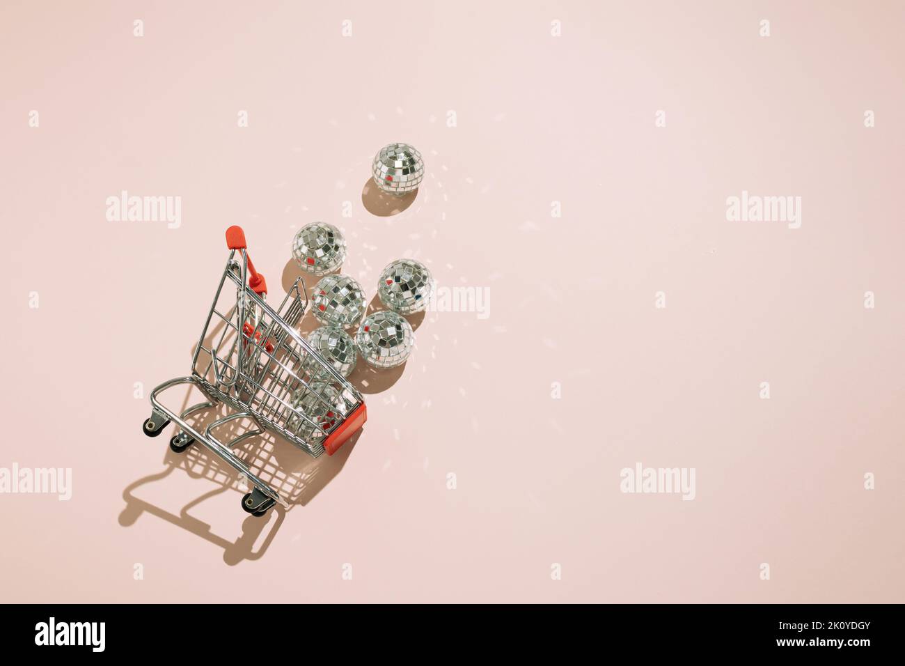 Overturned shopping cart with disco balls falling out on pink