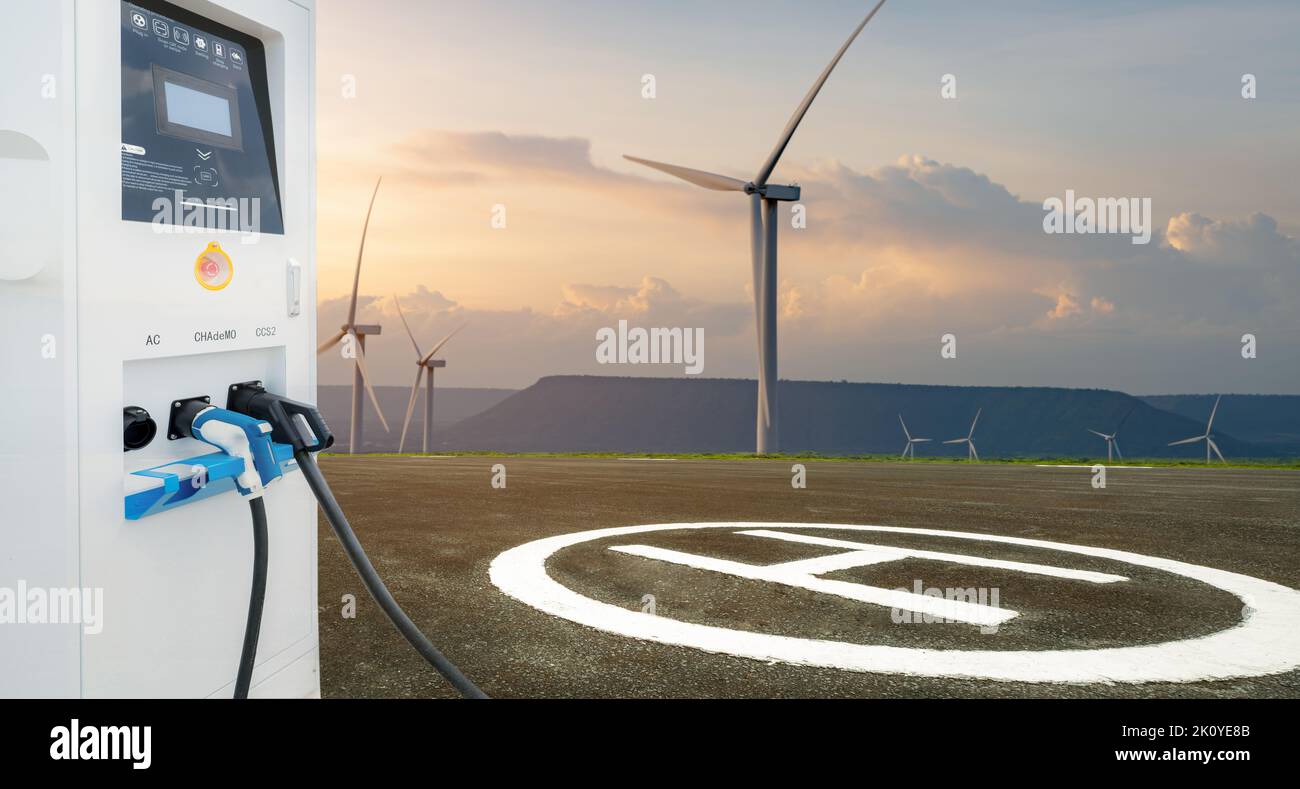 Electric vehicle charging station with asphalt helipad and wind turbines farm. Platform for helicopters. Sustainable and renewable energy. Green power Stock Photo