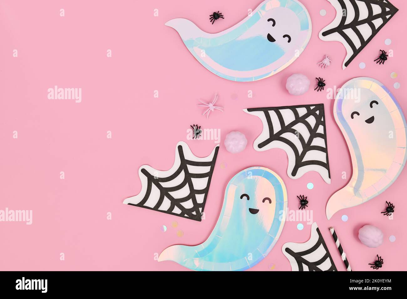 Cute pastel colored Halloween party flat lay with ghost shaped plates, spider web napkins and confetti on pink background Stock Photo