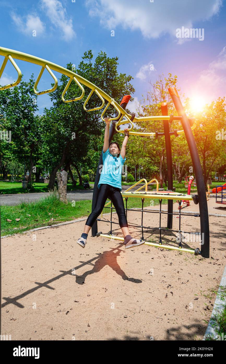 Cute child girl hanging hanging on monkey bars at the playground in park outdoor. Cute little girl having fun on summer garden. Stock Photo