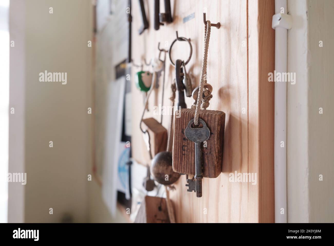 Vintage door key with a wooden keychain hangs on a hook on a board, on a blurred background.  Stock Photo
