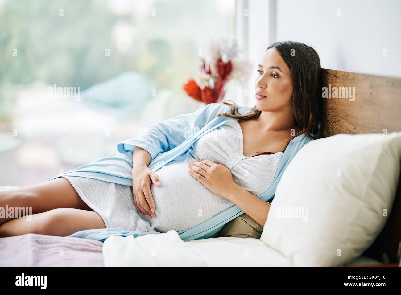 Portrait of happy pregnant woman relax lying in bed and touching her belly at home. Motherhood, people concept. Tender mood photo of pregnancy. Stock Photo