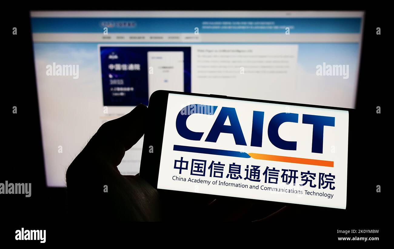 Person holding smartphone with logo of Chinese communications research institute CAICT on screen in front of website. Focus on phone display. Stock Photo