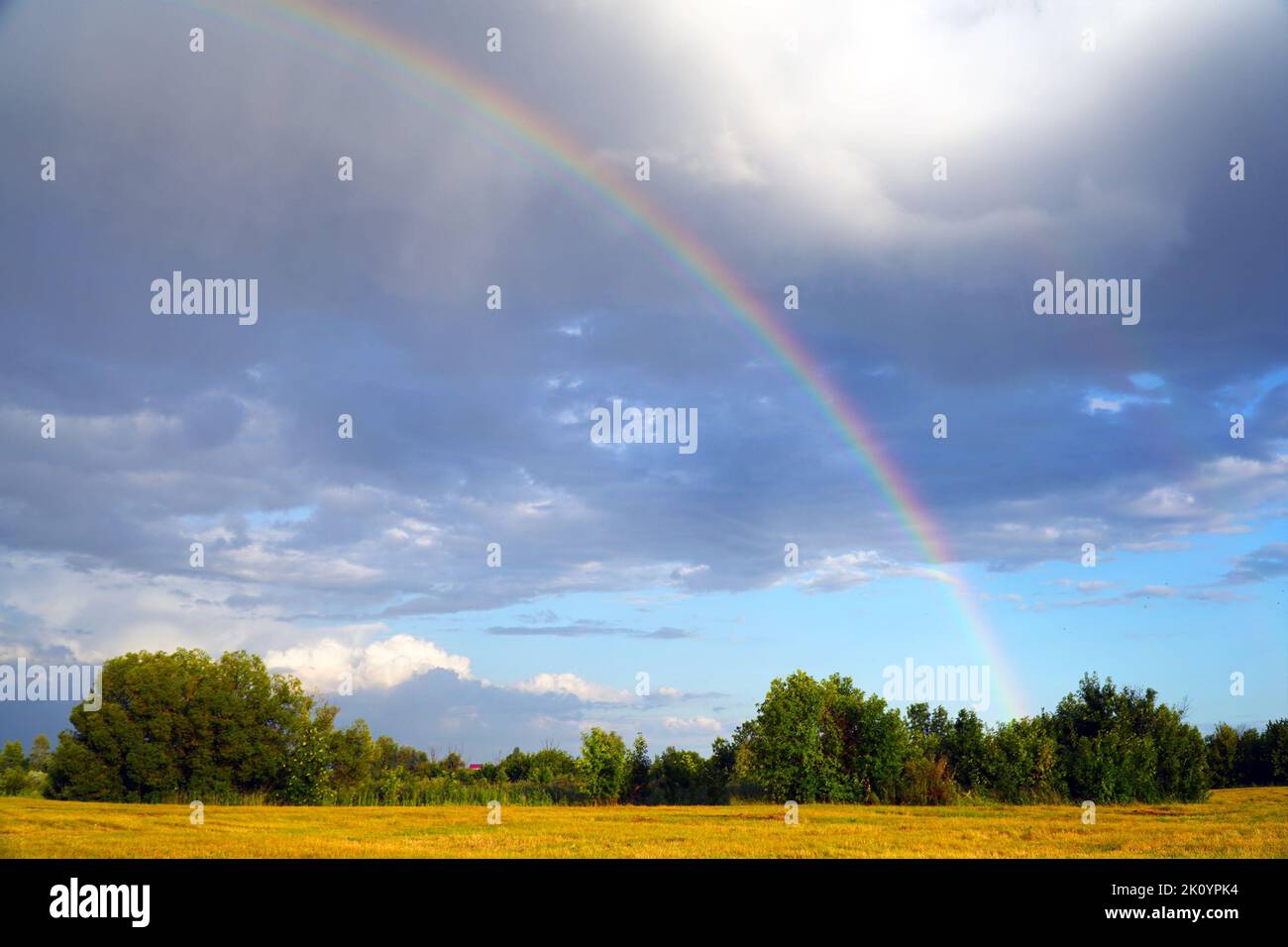 Rainbow on the background of storm clouds over a mown meadow Stock Photo