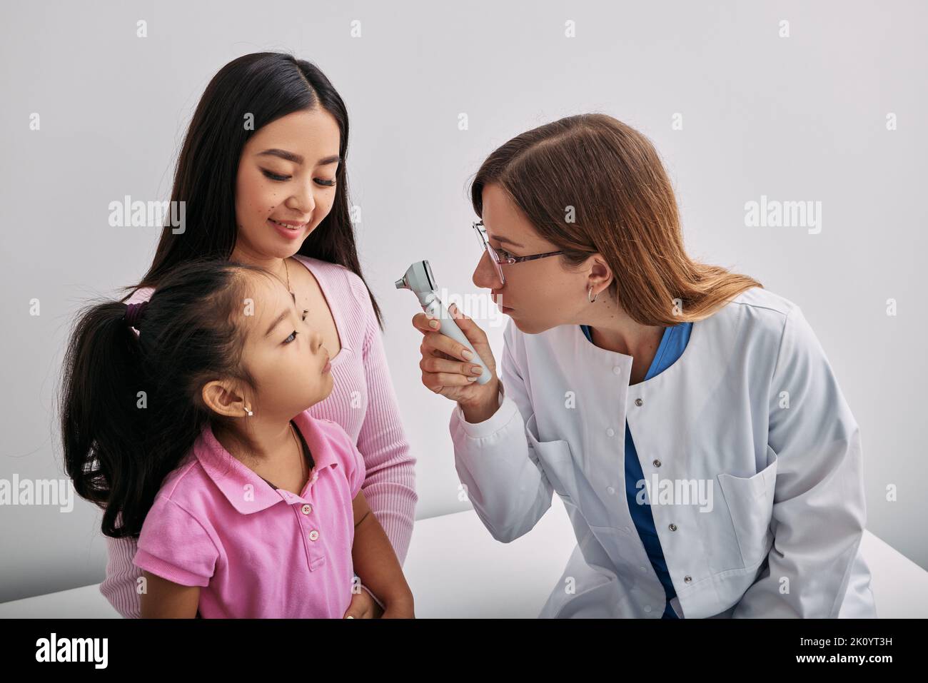 Doctor ophthalmologist using ophthalmoscope looking into eyes of Asian little girl who is sitting next to her mother. Checking child's vision Stock Photo