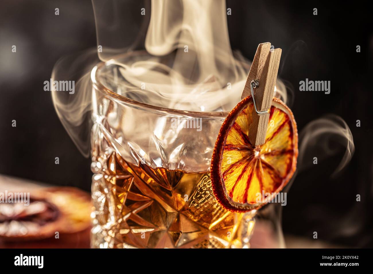 Smoked old fashioned rum cocktail with cubes of ice around on a dark background. Stock Photo