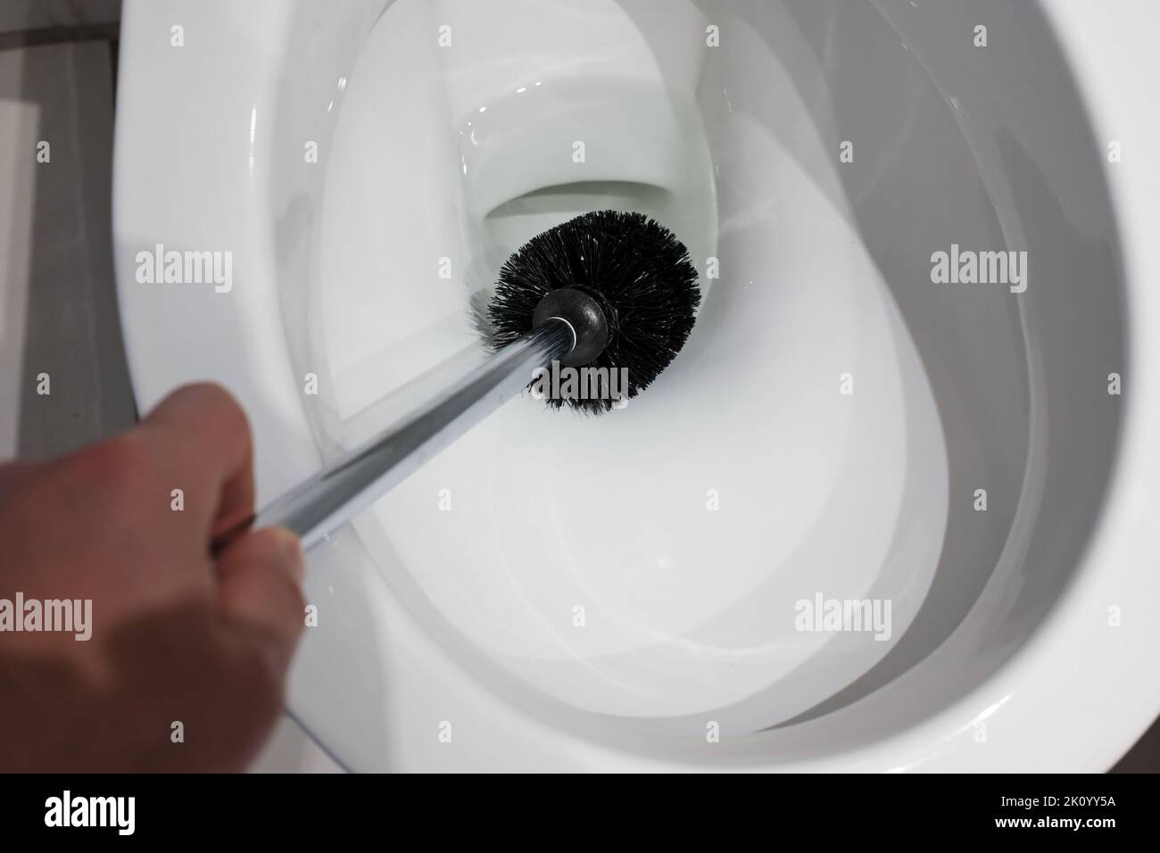 Hand cleans a white toilet bowl with a brush. Household chores. Top view. Close-up. Stock Photo