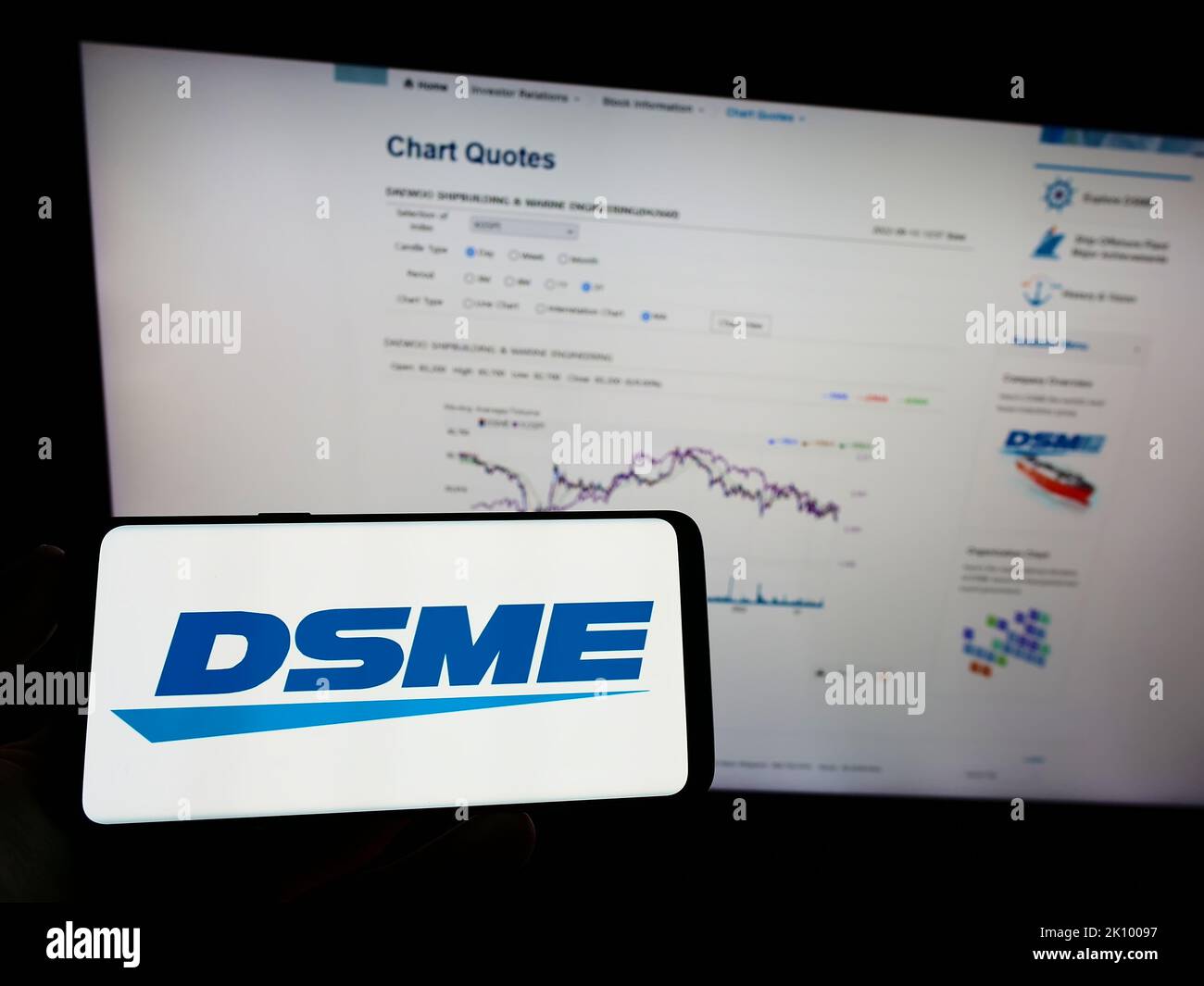 Person holding mobile phone with logo of Daewoo Shipbuilding and Marine Engineering (DSME) on screen in front of web page. Focus on phone display. Stock Photo