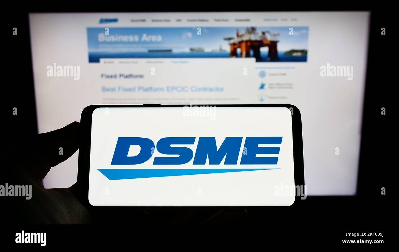 Person holding smartphone with logo of Daewoo Shipbuilding and Marine Engineering (DSME) on screen in front of website. Focus on phone display. Stock Photo