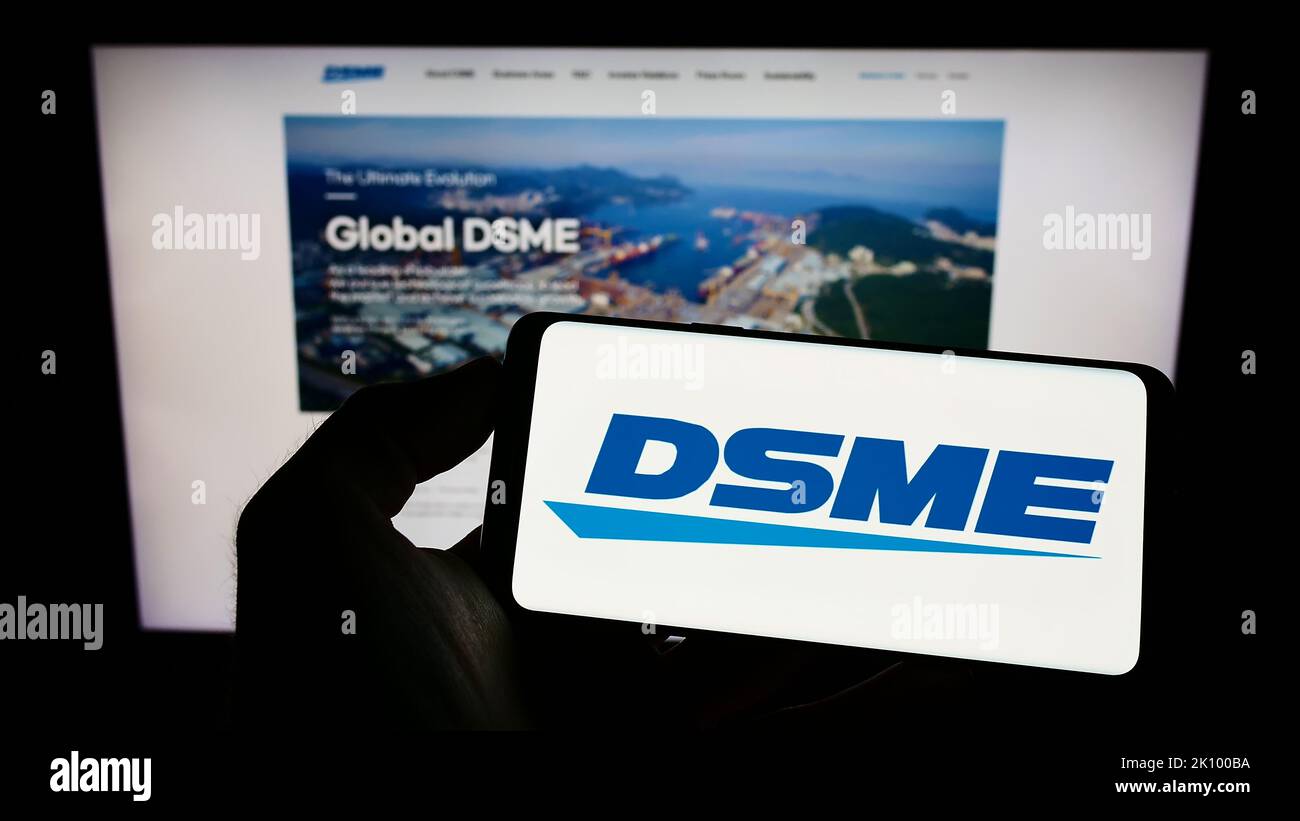 Person holding cellphone with logo of Daewoo Shipbuilding and Marine Engineering (DSME) on screen in front of webpage. Focus on phone display. Stock Photo
