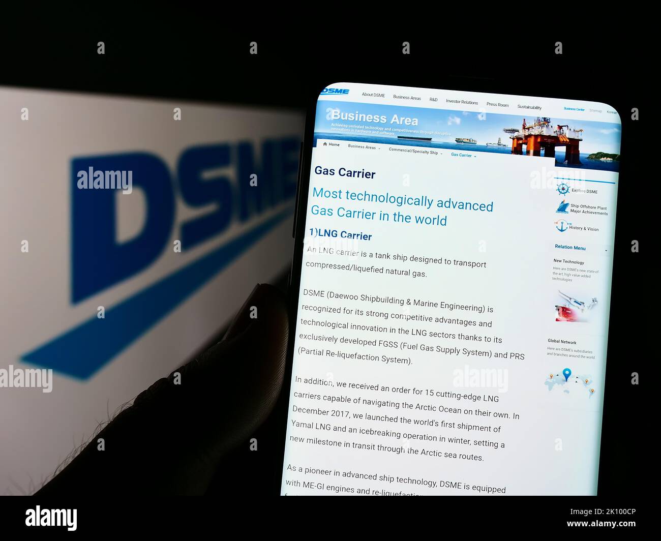 Person holding cellphone with webpage of Daewoo Shipbuilding and Marine Engineering (DSME) on screen with logo. Focus on center of phone display. Stock Photo
