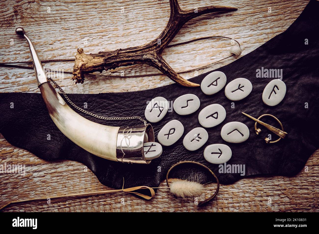 Above view of rune stones with various viking era style objects, drinking horn, bronze brooch, glass bead on leather string. Ancient divination. Stock Photo