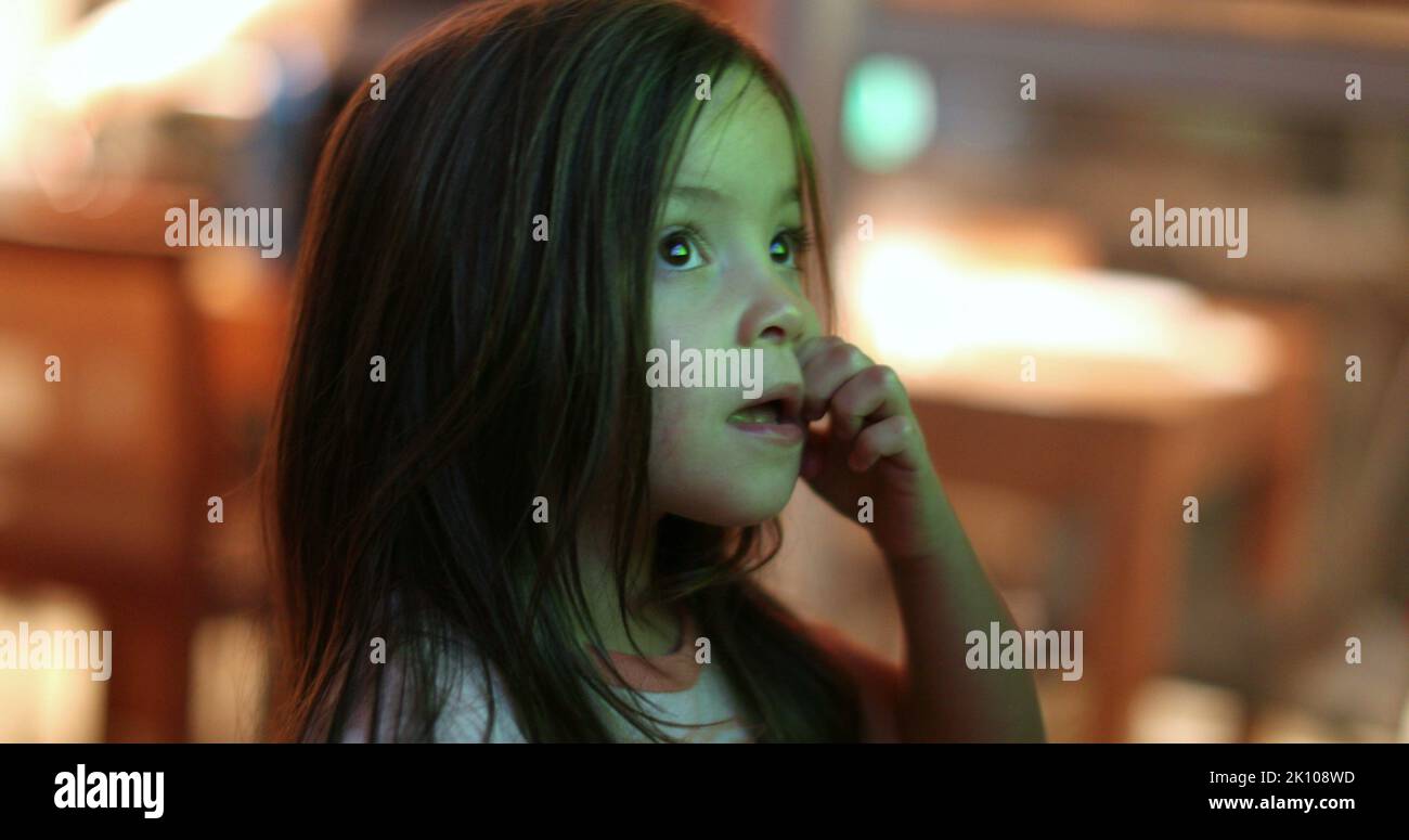 Little girl child watching TV screen at night. Small kid hypnotized