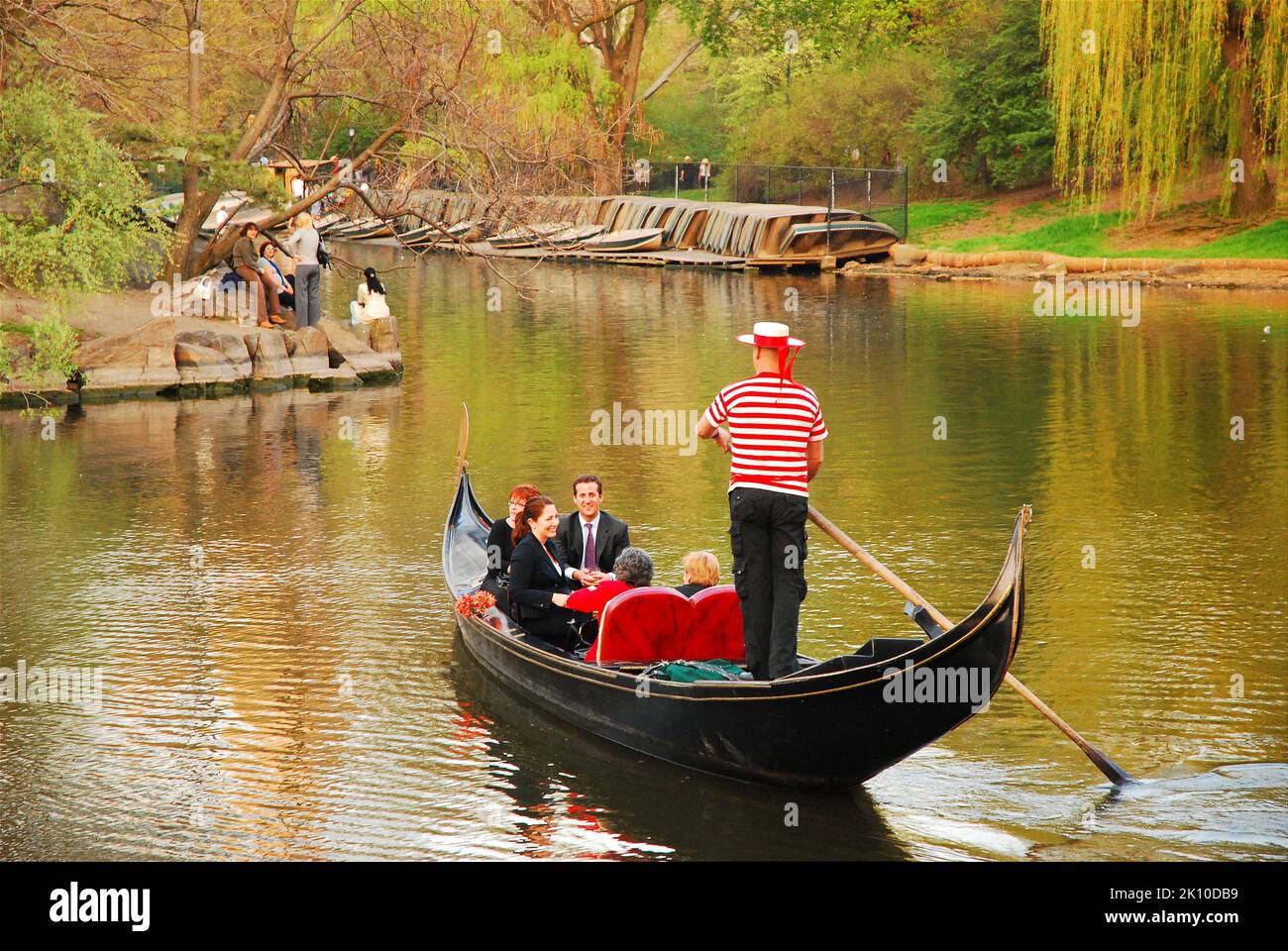 A Venetian gondolier steers a gondola across the lake in New York City Central park, providing a romantic setting for the two couples on board Stock Photo