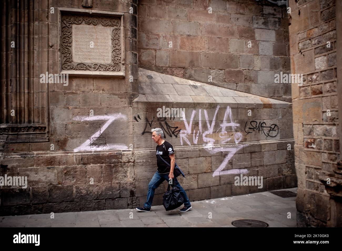 A man walks past a pro-Russian graffiti drawn on the walls of Barcelona's Cathedral, Spain. Russia-Ukraine war has highly impacted European energy and food markets. EU countries are coordinating actions to tackle rising prices and scarcity of supplies. Stock Photo
