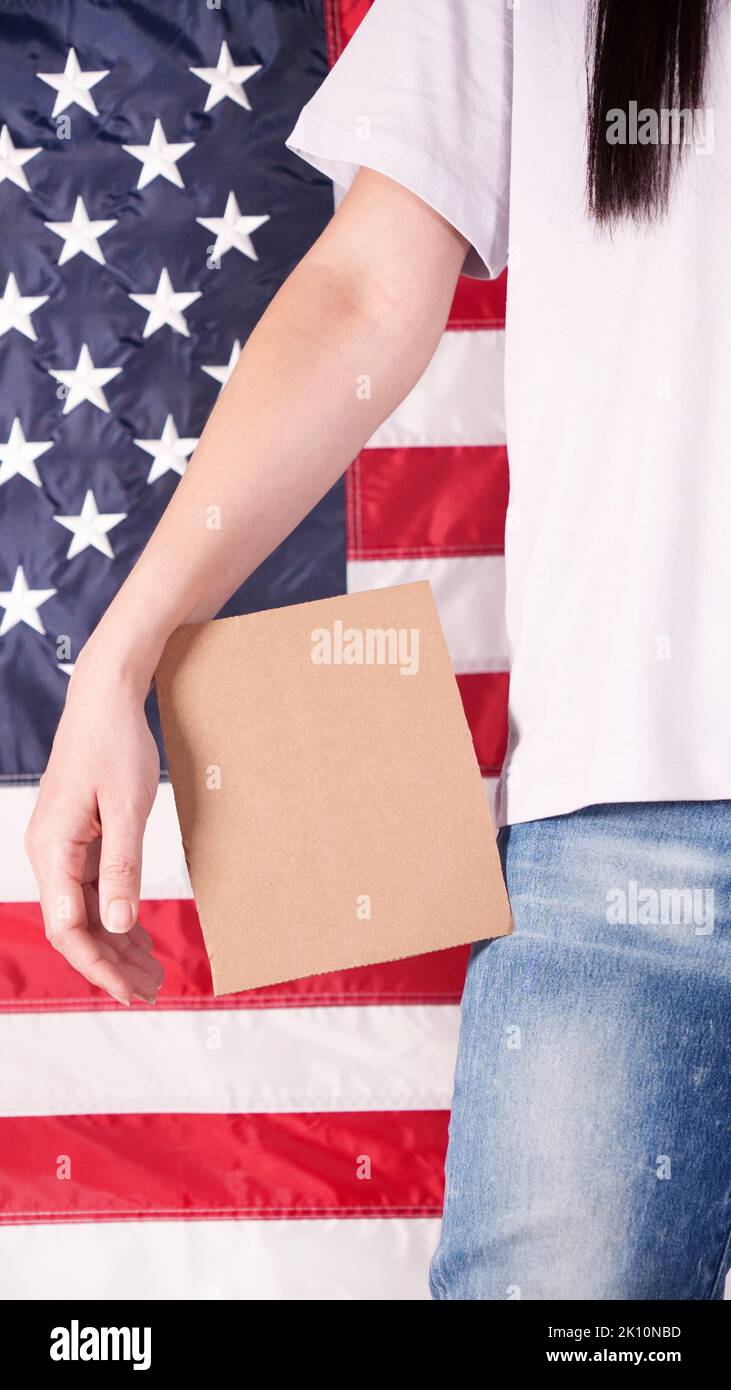 Young woman holds empty cardboard with Space for Text sign against American flag on background. Girl protesting anti-abortion laws. Feminist power. Wo Stock Photo
