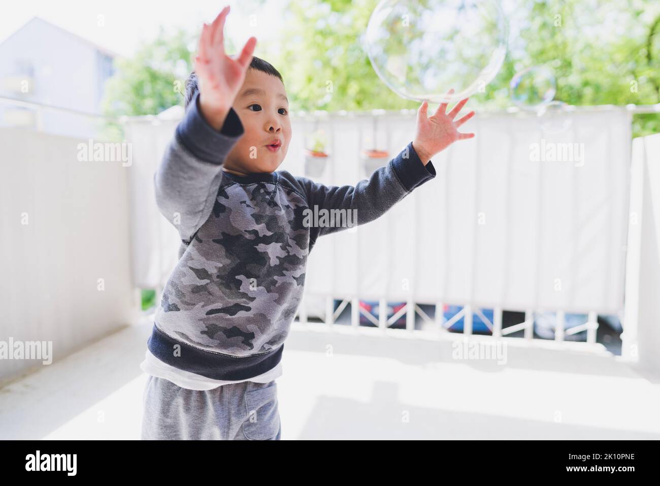 A toddler chasing a bubble on a balcony Stock Photo