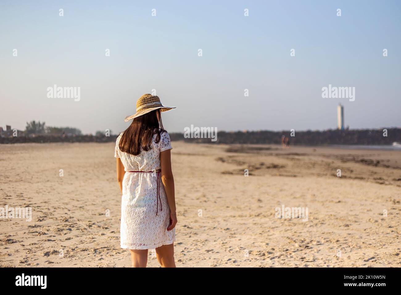 Pregnant woman in lace dress and hat, back to back, walking on the beach Stock Photo