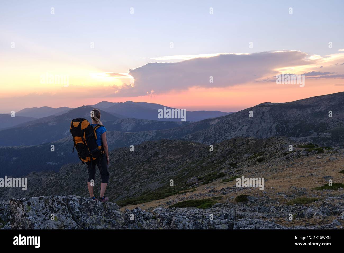 A Female backpacker admiring mountains at sunset Stock Photo