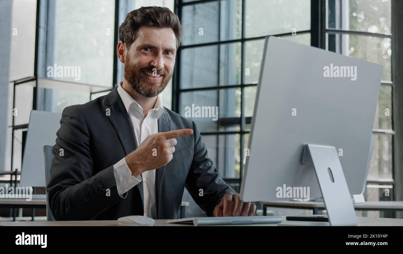 Adult Caucasian bearded businessman in office space working with online computer app website showing with index finger pointing with forefinger to Stock Photo