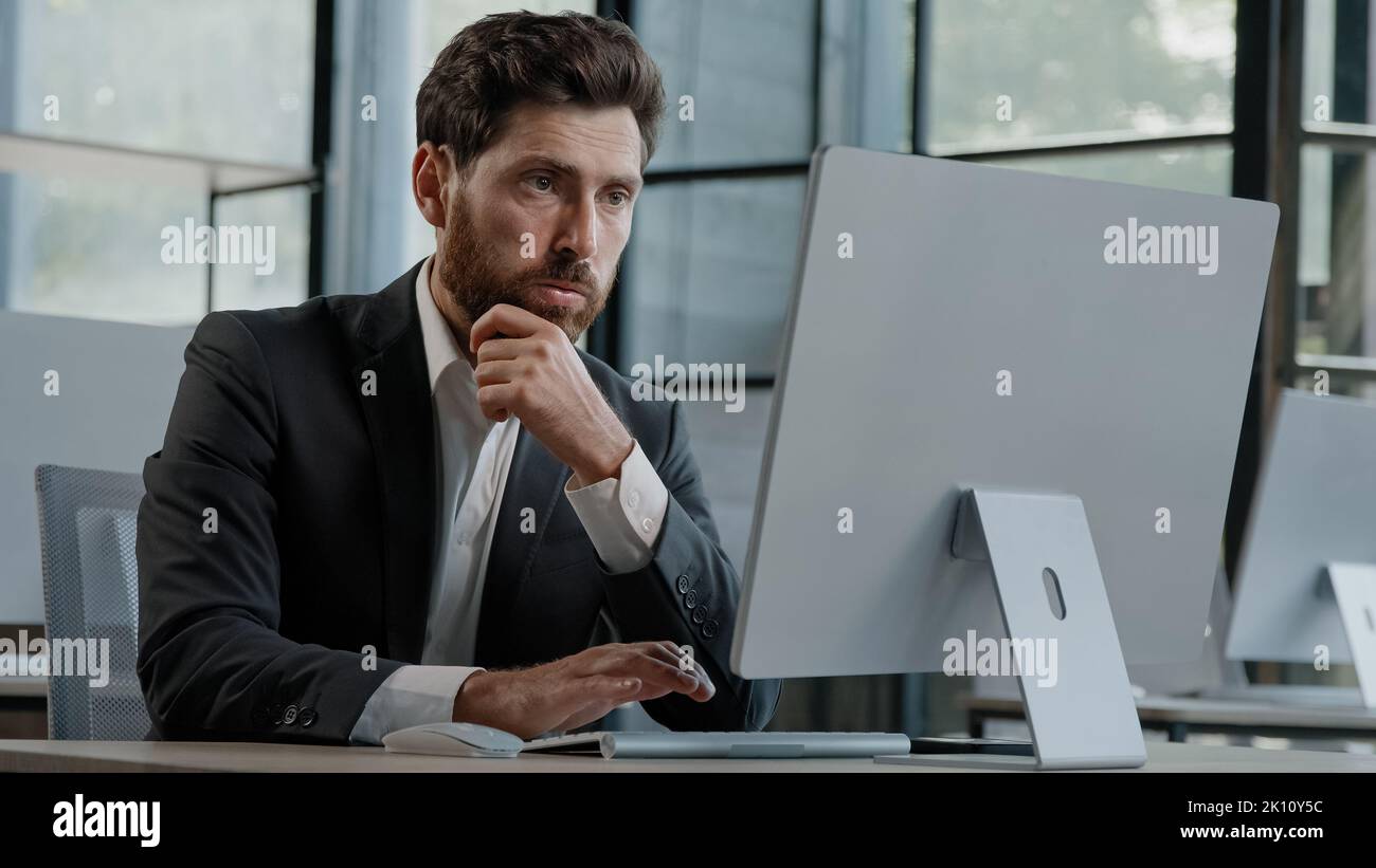 Focused Caucasian bearded adult 40s man CEO company worker manager boss businessman working on computer in office searching solution of problem decide Stock Photo