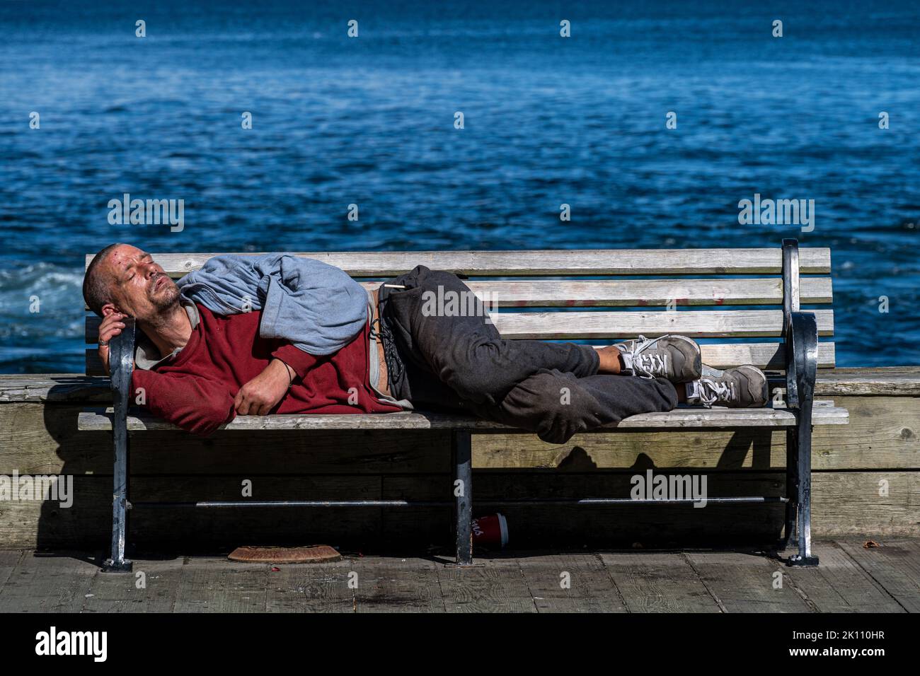 Halifax, Nova Scotia, Canada -- Sept 14, 2022. Photo of a young man sleeping on a waterfront bench on the Halifax Harbour boardwalk. Stock Photo