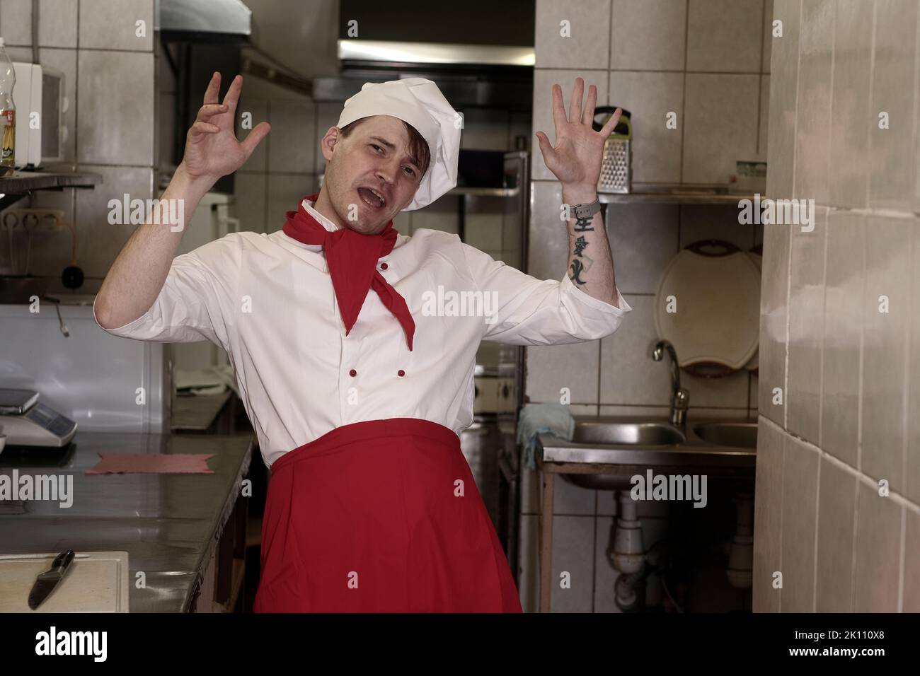 Young happy man dressed as chef dancing in kitchen in restaurant. Male cook in uniform having fun, rejoicing at ordering Stock Photo