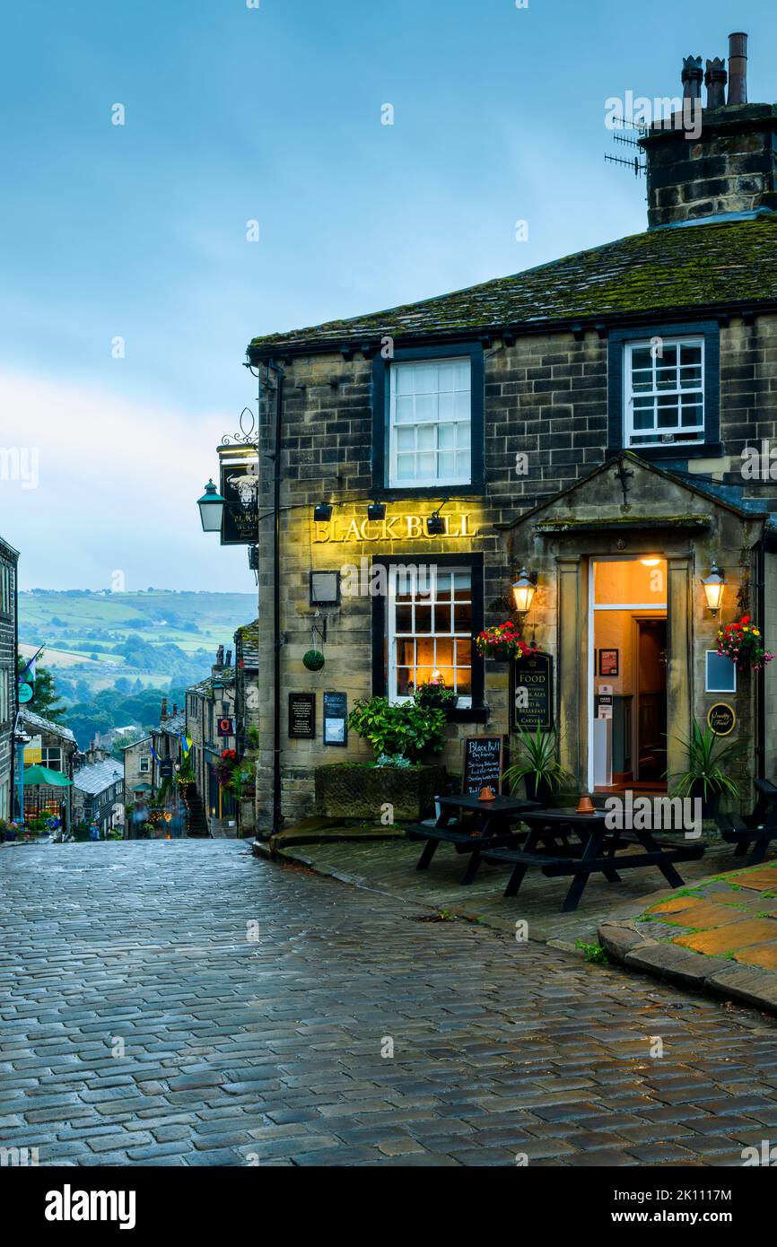Haworth Main Street (steep hill, old buildings, blue hour evening light, historic Bronte sisters' village, Grade 2 pub) - West Yorkshire, England, UK. Stock Photo