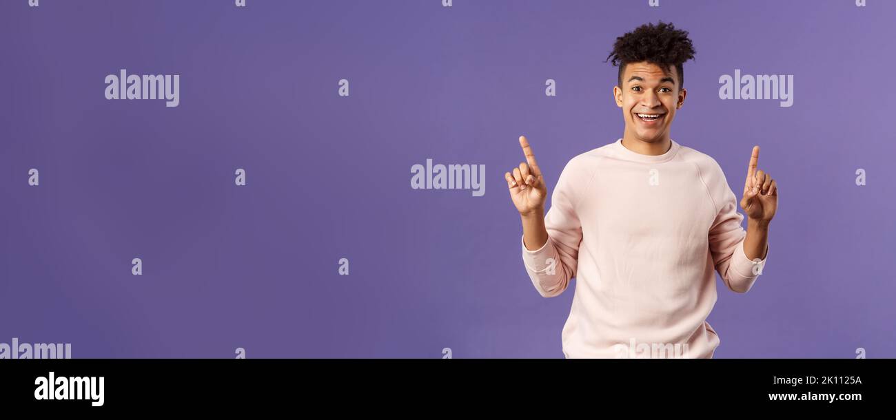 Portrait of charismatic lively young man heard about good deal, asking question intrigued, pointing fingers up, smiling upbeat at camera, look with Stock Photo