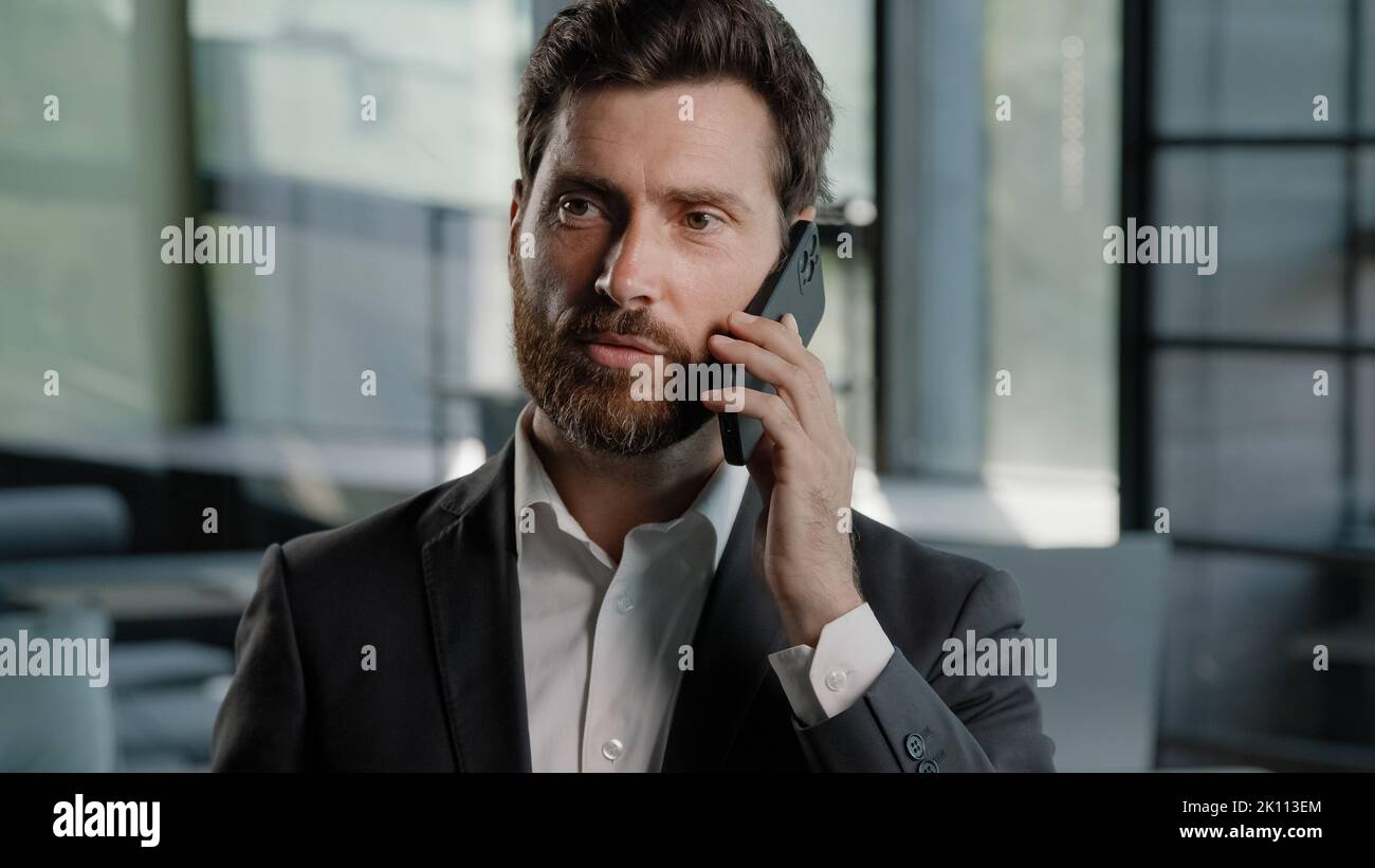 Bearded Caucasian middle-aged adult business man talking phone at office explain negotiate virtual sales conversation using mobile male professional Stock Photo