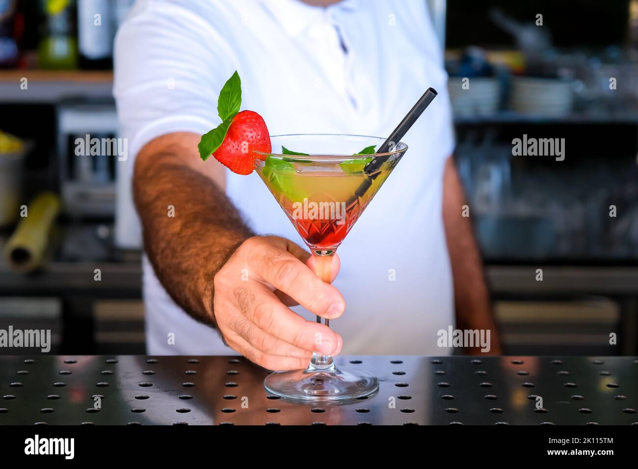 Hand of bartender serving fresh yellow, red summer fruit cocktail at bar counter on sunny day. Selected focus, shallow depth of field. Stock Photo