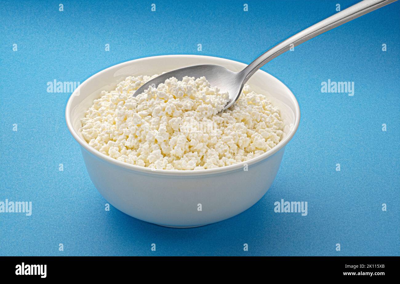 Bowl of cottage cheese with spoon on blue background Stock Photo