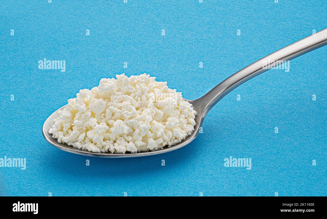 Cottage cheese in spoon on blue background Stock Photo